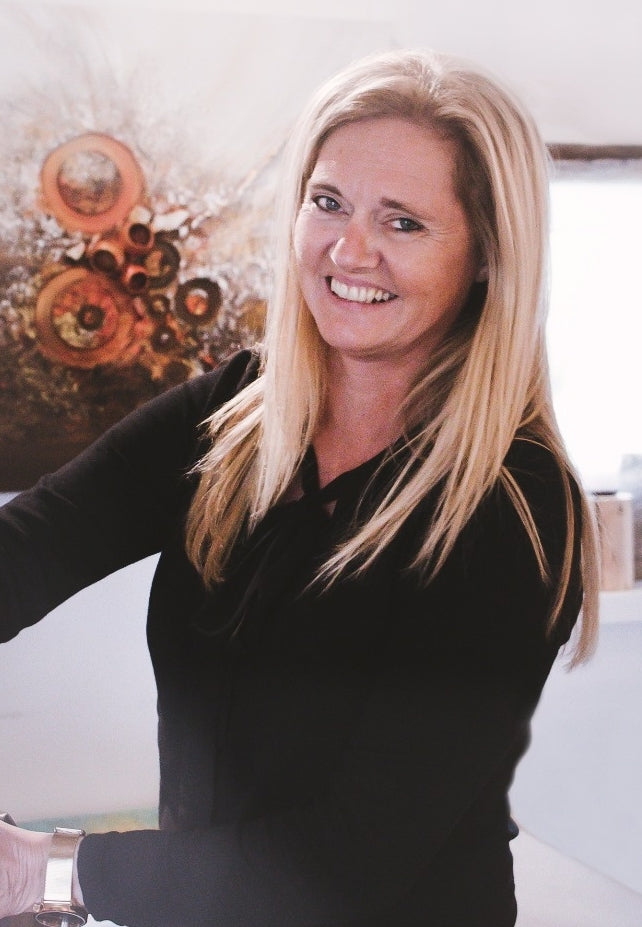 Heidi Douven, zaakvoerder van Kunst voor iedereen, glimlachend voor een van haar werken in de kunstschuur in Knesselare
