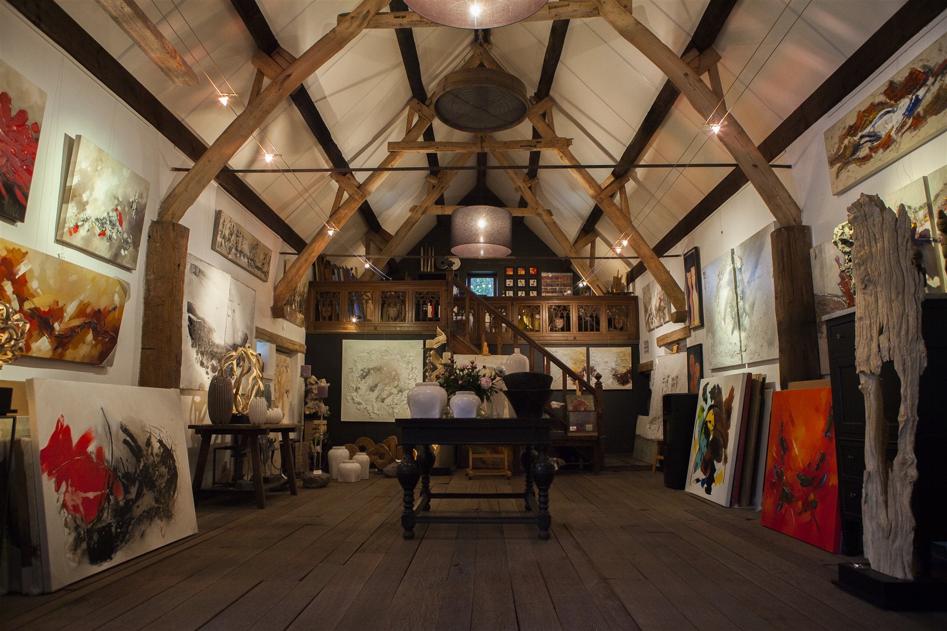Het interieur van de kunstschuur in Knesselare, met schilderijen langs de muren en warme sfeerverlichting